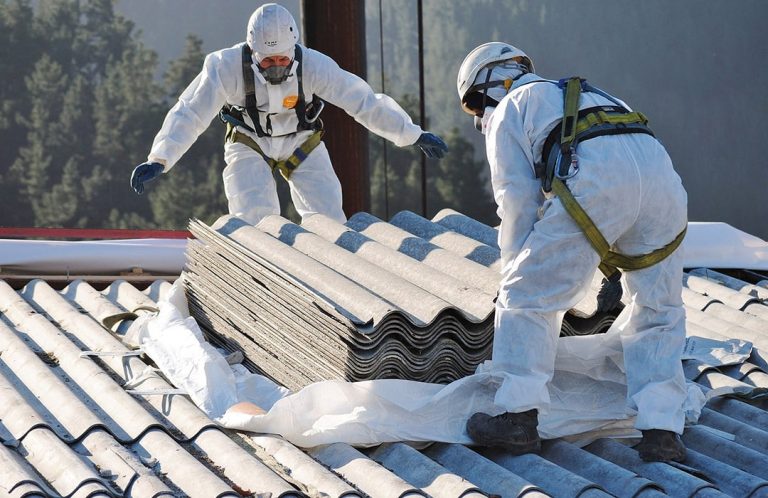 Asbestos experts in protective gear removing asbestos sheets from a roof