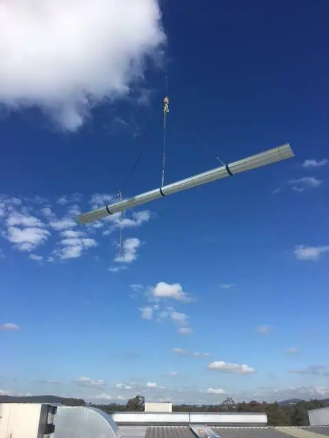 Metal panels being lifted into place on a commercial roof by a crane